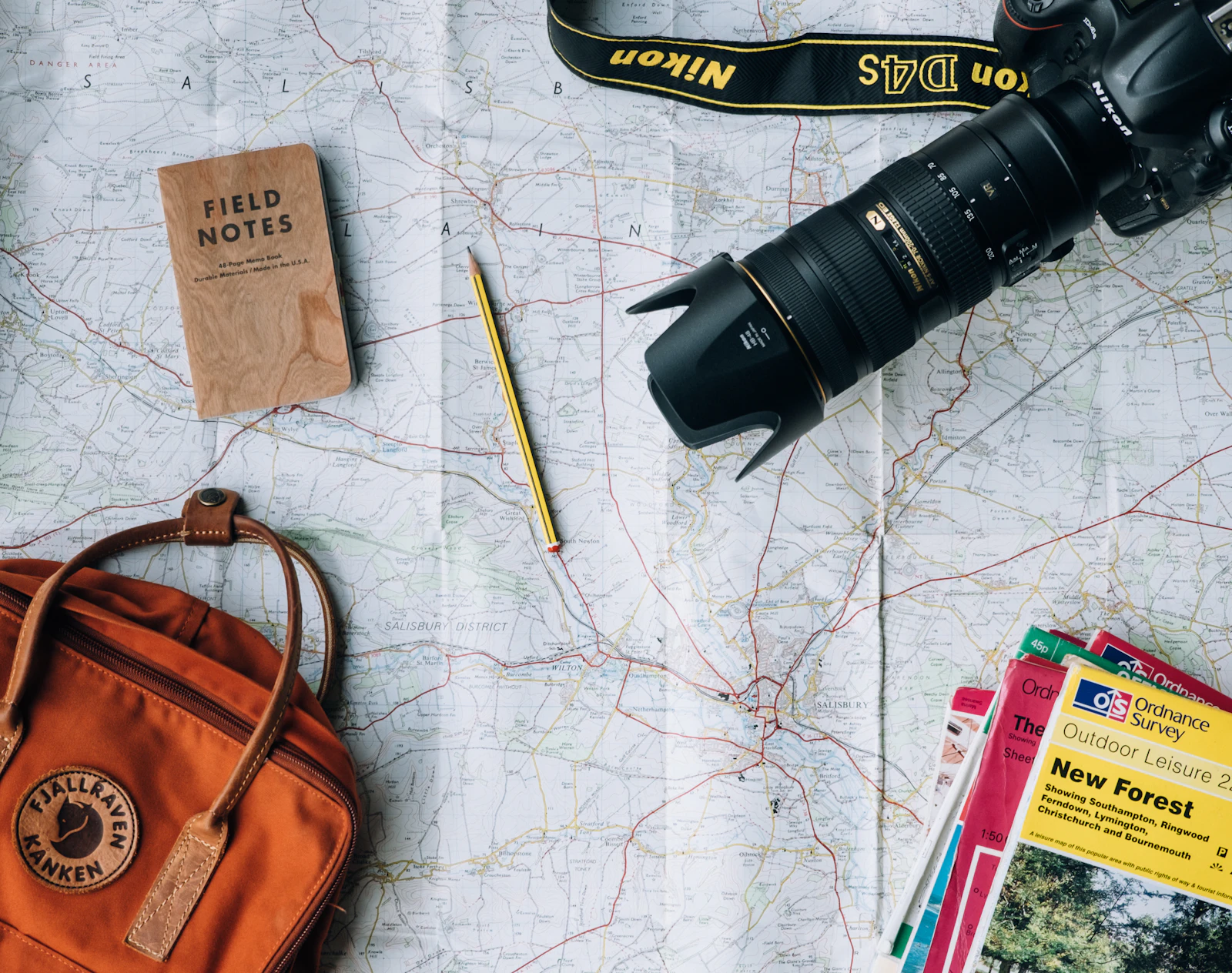 Flat lay of a paper map, camera, notebook and small backpack laid out for trip planning