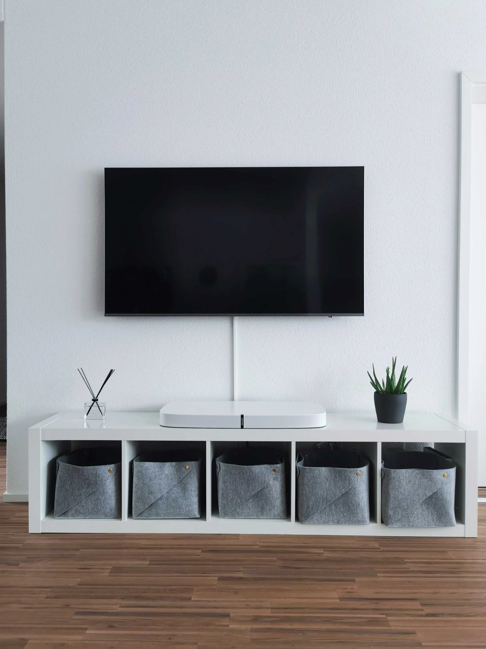 Minimalist living room with a wall-mounted television and storage bench on hardwood flooring