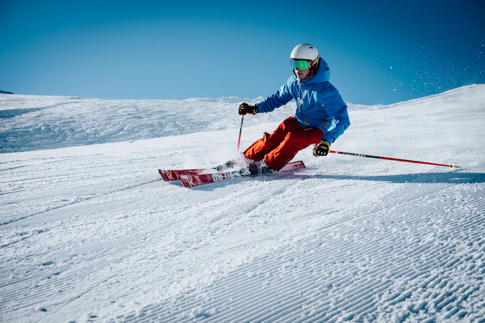 Skier carving down a steep powder slope wearing ski goggles at golden hour
