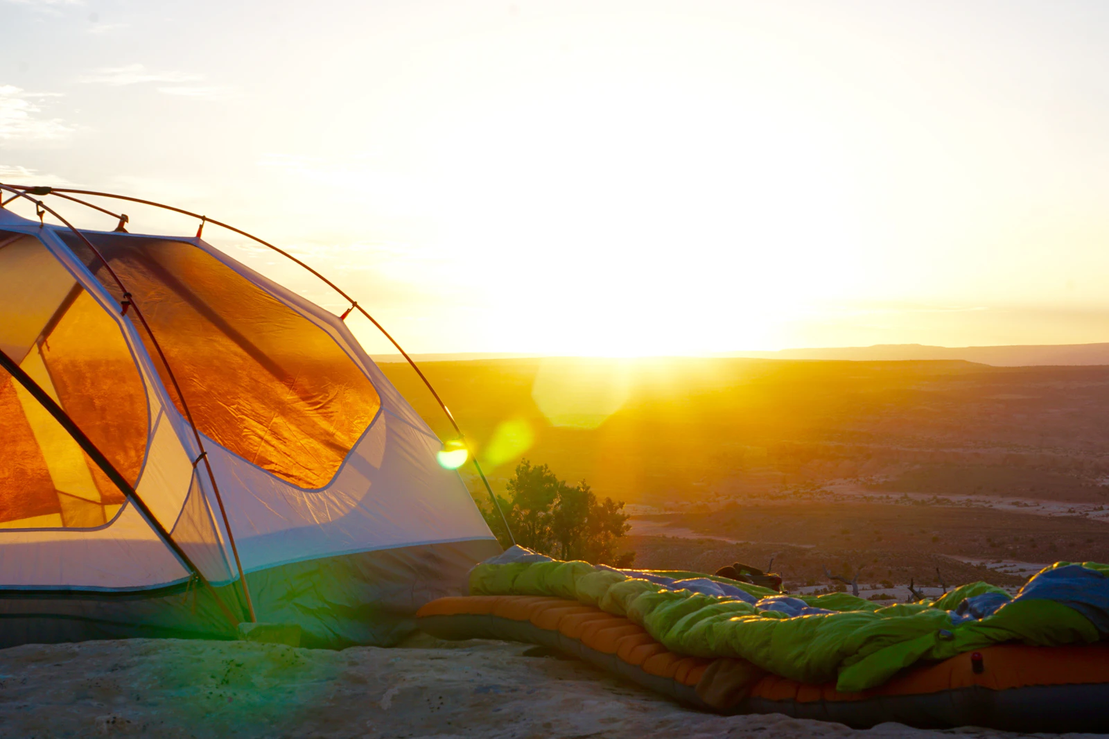 Tent and an unrolled sleeping bag on a ridge with the sun low on the horizon
